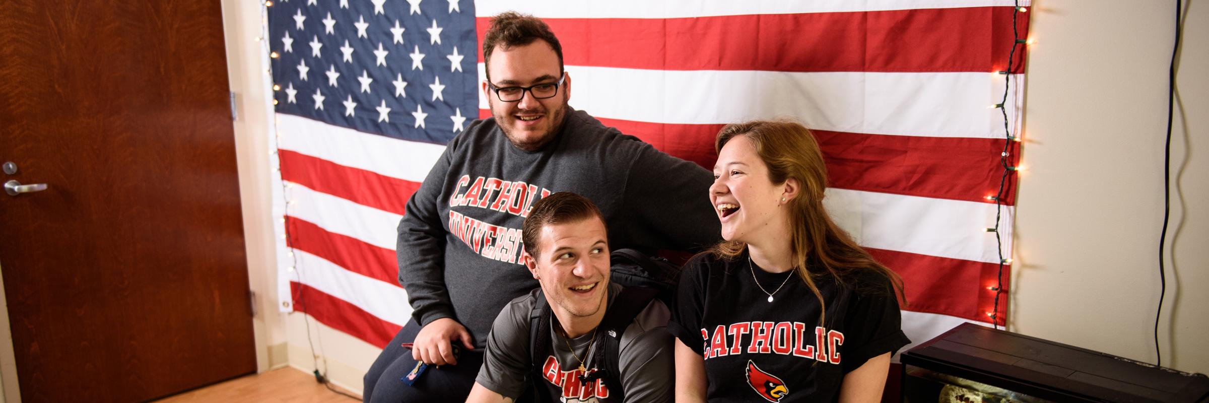 Students smiling in a dorm with a U.S. flag behind them