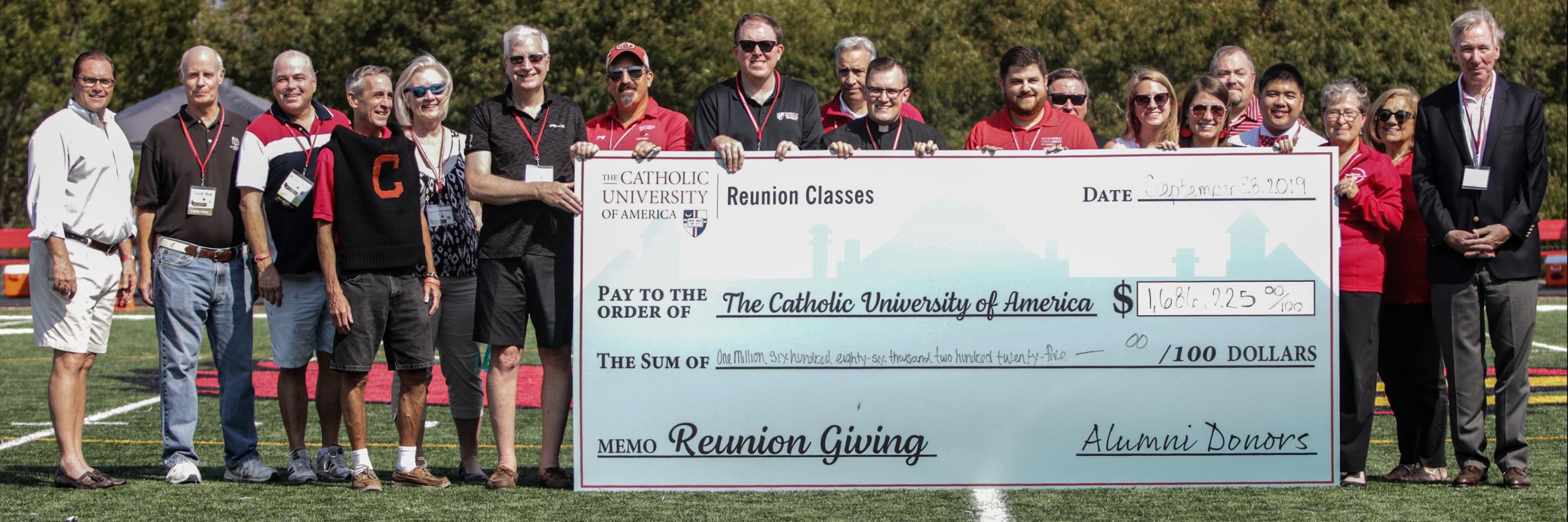 Reunion alumni holding a large check on a football field