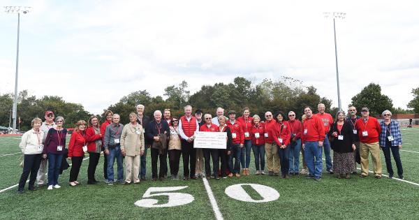 Reunion alumni holding a large check on the football field
