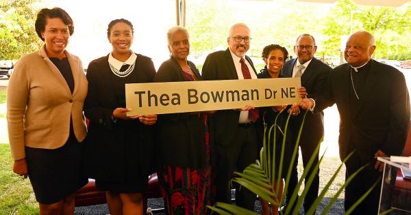 People smile holding a sign for Thea Bowman Drive