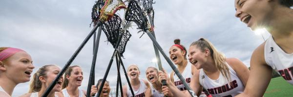 Women's lacrosse players cheer and hold their sticks high