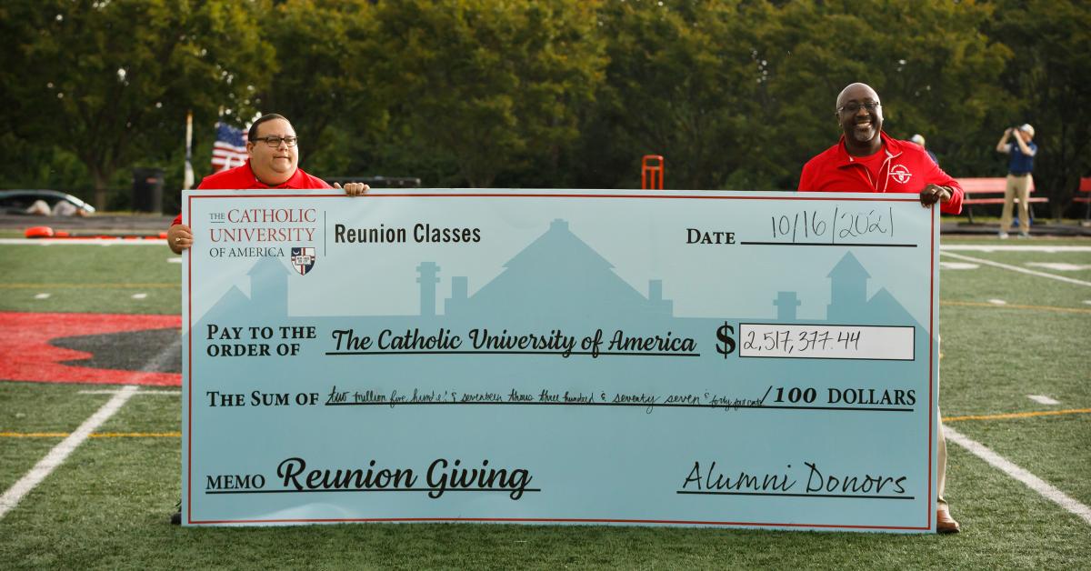 Members of the Board of Directors hold a giant check on the football field